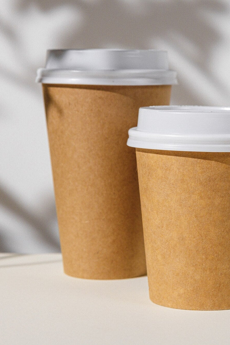 Two brown paper cups with white lids on a light background